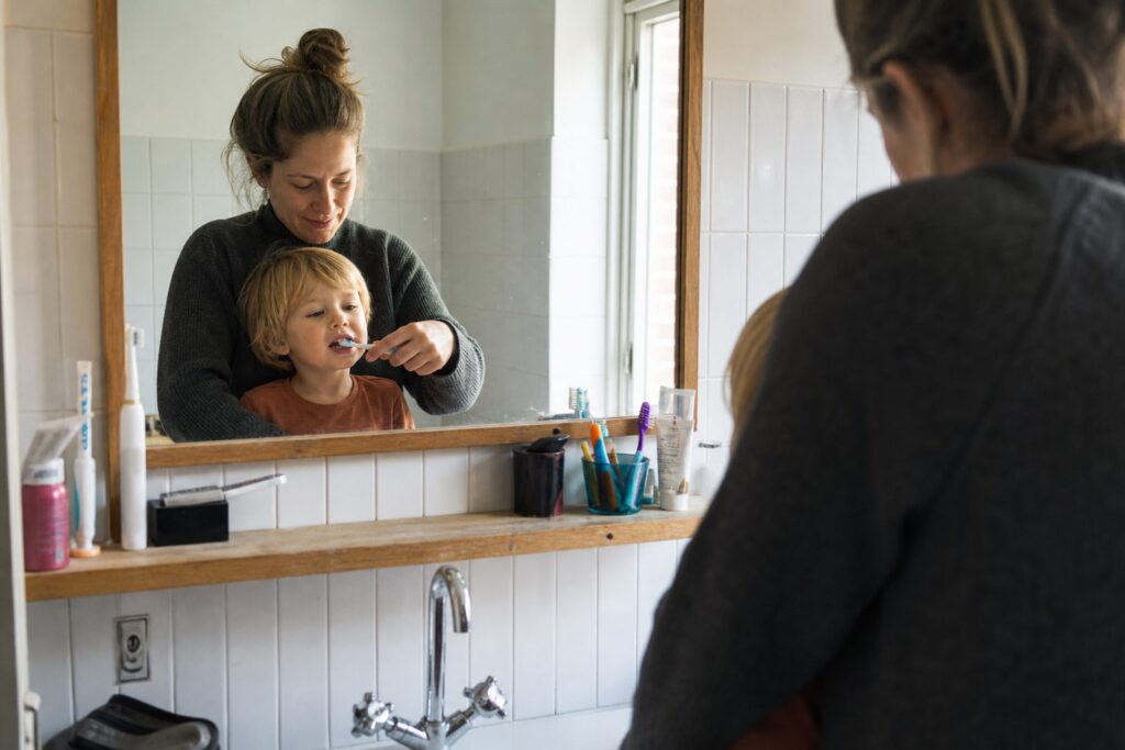 Ouder poetst de tanden van een peuter voor de badkamerspiegel