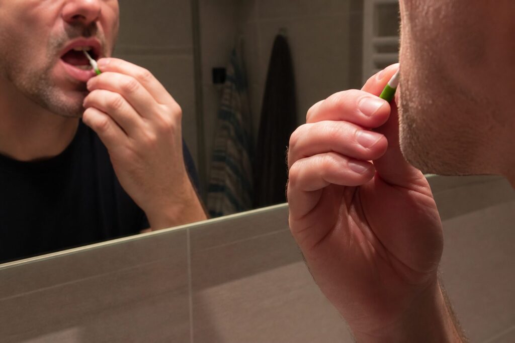 Hand gebruikt een interdentale rager boven de wastafel